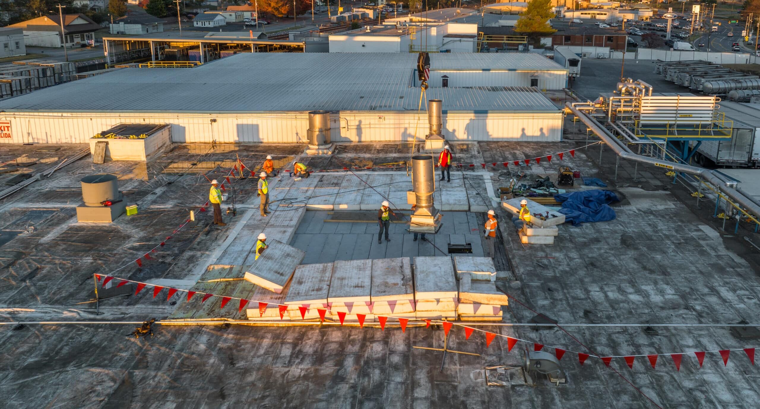 aerial photo of workers replacing panels on the roof of a plant